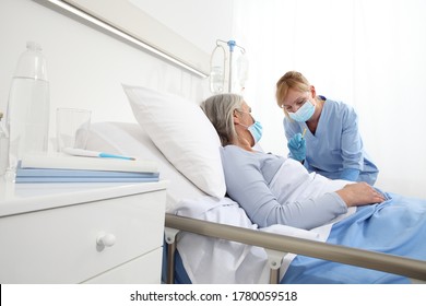 Die Krankenschwester mit der Spritze injiziert den Impfstoff an ältere Patientinnen, die im Krankenhausschlafzimmer liegen und Schutzhandschuhe und ärztliche chirurgische Maske tragen, das Schutzkonzept Coronavirus covid 19
