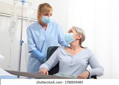 Die Krankenschwester nimmt Komfort ältere Frau im Rollstuhl, die chirurgische Schutzmasken im Krankenhausraum trägt, Konzept der Isolierung von Corona-Virus-Covid 19