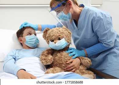 Nurse Takes Care Of The Patient Child In Hospital Bed Playing With Teddy Bear, Wearing Protective Masks, Corona Virus Covid 19 Protection Concept, 