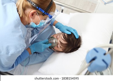 Nurse Takes Care Of The Patient Child In Hospital Bed Playing With Teddy Bear, Wearing Protective Masks, Corona Virus Covid 19 Protection Concept, 