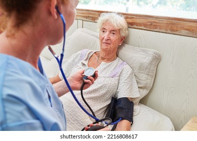 Nurse Taking Blood Pressure Of A Bedridden Elderly Woman In Bed In Nursing Home