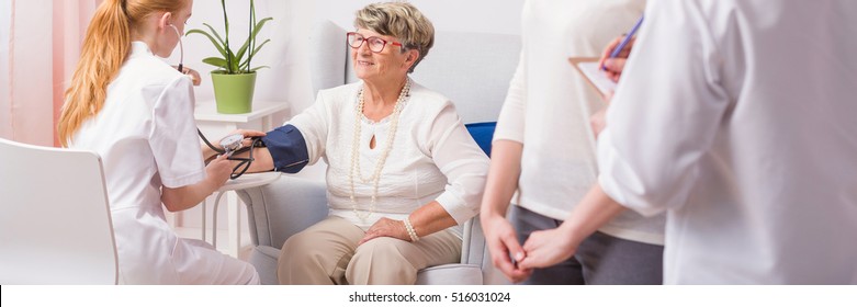 Nurse Taking Blood Pressure Of A Senior Woman During Home Visit, Panorama