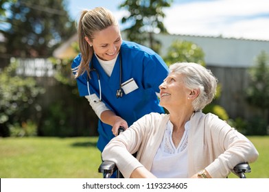 Nurse taking care of old woman in wheelchair outdoor. Friendly doctor caring about elderly disabled woman in wheelchair. Happy elderly woman with her caregiver at nursing home park.