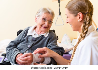 Nurse Taking Care Of Senior Woman In Retirement Home Bandaging A Wound