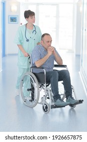 Nurse Taking Man Patient In Wheelchair At Hospital Corridor