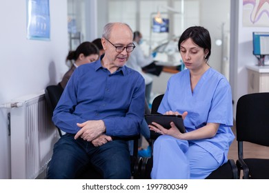 Nurse Taking Notes On Tablet Pc Discussing With Senior Patient In Dental Office, Explaining Diagnosis. Assistant Filling Writing Healthcare Form. Dentistiry Hospital.