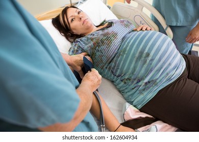 Nurse Taking Pregnant Woman's Blood Pressure In Hospital Room