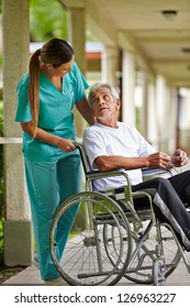 Nurse Talking To Elderly Man In Wheelchair In A Nursing Home