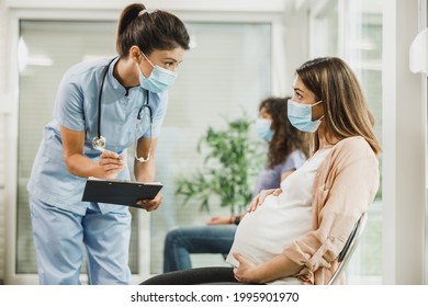Nurse talking to young pregnant woman and taking notes before covid-19 vaccine at hospital waiting room.