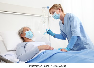 nurse with thermometer measures fever on elderly woman patient lying in the hospital room bed, wearing protective gloves and medical surgical mask, coronavirus covid 19 protection concept
