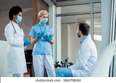 Nurse And Two Doctors Talking In A Lobby And Wearing Protective Face Masks Due To Coronavirus Pandemic.