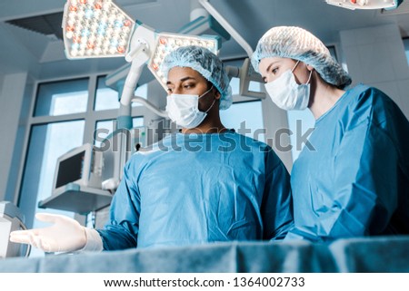  nurse in uniform and mask and doctor pointing with fingers in operating room 