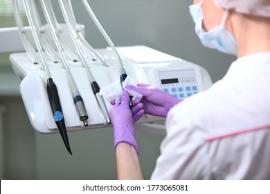 A nurse in uniform and a medical mask wipes the dental unit. Back view. Gloved hand.Disinfection in the dental office. Copy of the space. Gray background.