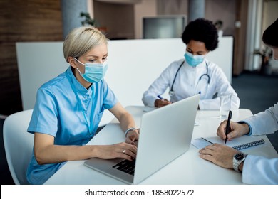 Nurse using laptop while wearing face mask and working with her colleagues at the clinic.