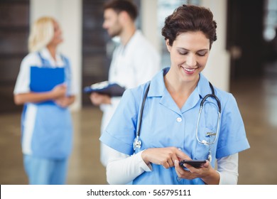 Nurse Using On Mobile Phone With Doctors Discussing On Background