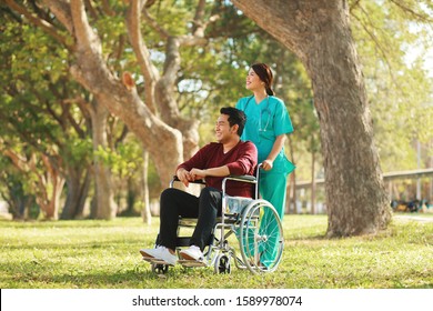 nurse walking with a man on wheelchair at nature park of hospital.