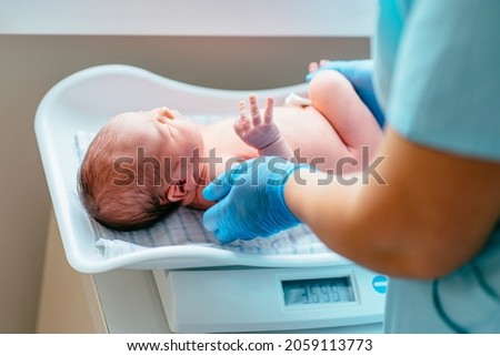 A nurse weighs on the scales a newborn baby at hospital. Health care concept.