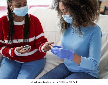 Nurse Woman Takes Blood From A Senior African Patient At Home For The Diabetes Exam While Wearing Surgical Face Mask For Coronavirus Outbreak