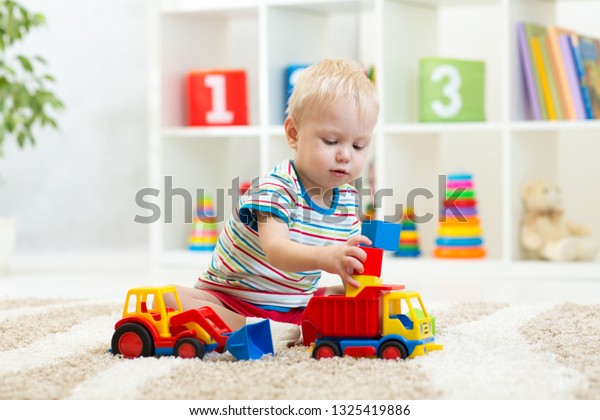 Nursery baby boy plays block and car toys sitting\
on carpet indoors