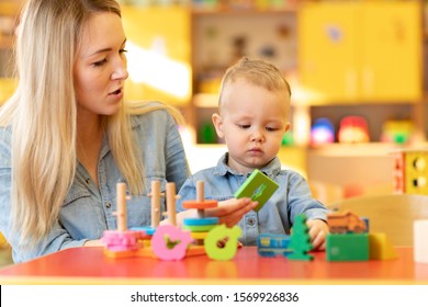 Nursery baby and carer play at table in kindergarten
