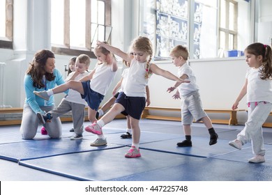 Nursery Teacher Helping One Of Her Students During A Physical Education Lesson.