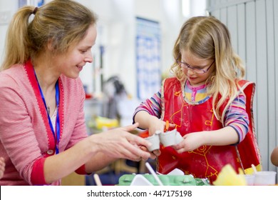 Nursery teacher helping a student cut an egg box in their crafts lesson.