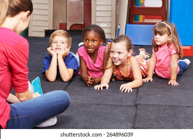 Nursery teacher reading story book to group of kids in kindergarten