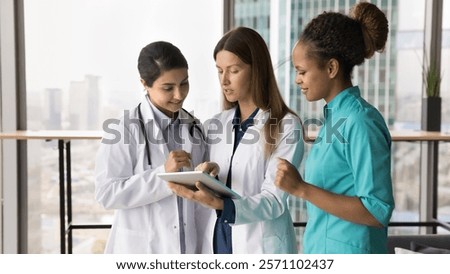 Nurses and GP dressed in uniforms standing in clinic office, talking, using tablet at workplace. Review latest updates, learn new platform, telemedicine application, share opinion regarding treatment