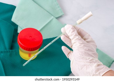 A nurse's hand holds an urinary catheter on a table where there is a container with urine for analysis with green hospital cloth.