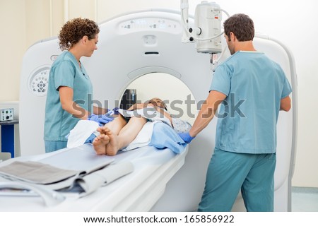 Nurses preparing female patient for CT scan in examination room