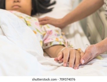 Nursing Caretaker Concept With Child Patient (girl Kid) Sleeping In Bed With Family Caregiver, Nurse Or Parenting Mother's Hand Support In Blur Medical Hospital Or Clinic Background (focus On Hand)