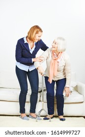 Nursing Helps Old Woman Getting Up From Sofa In Retirement Home