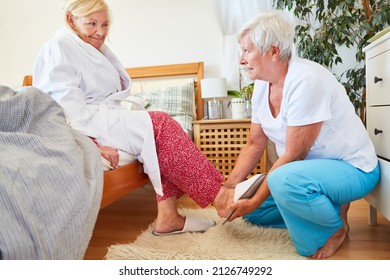 Nursing service woman helps senior citizen in nursing home to put on slippers at home