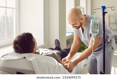 Nursing staff at clinic or hospital gives intravenous vitamin drip or medicine infusion to patient. Nurse personnel inserts venous IV line needle in arm vein of adult man lying on bed in medical ward