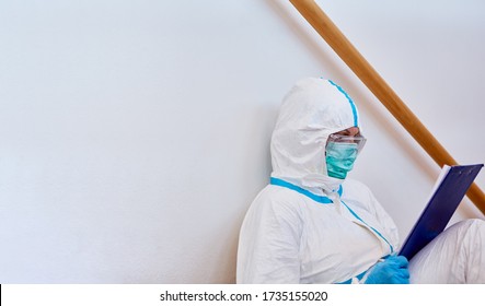 Nursing staff in clinic in protective clothing studies list on clipboard during break on floor during coronavirus epidemic - Shutterstock ID 1735155020