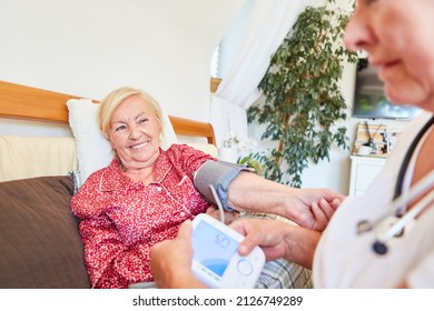 Nursing Woman Or Geriatric Nurse Taking Blood Pressure Measurements At Home Or In A Nursing Home