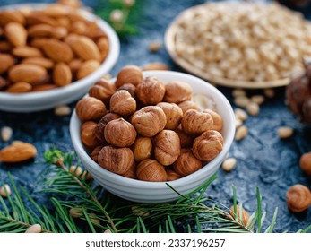 Nut assortment. Hazelnuts, almonds, pine nuts in plates stand on table with spruce branches. Top view. Background.