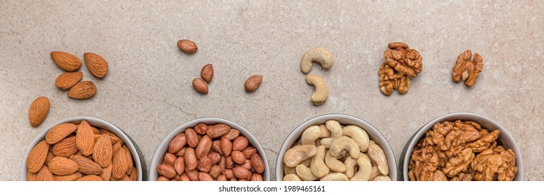 Nut background. Banner for large format printing, advertising and website design. Nuts of different varieties lie in bowls on a stone countertop, top view. Peanuts, cashews, almonds, walnuts.