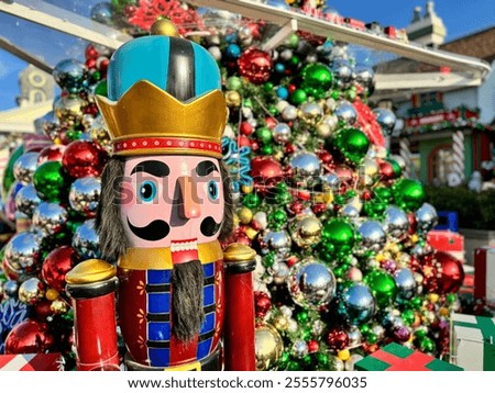 A Nutcracker puppet soldier stands in front of a Christmas tree decorated with colorful balls.