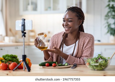 Nutrition Coach. Smiling Black Lady Recording Video Recipe In Kitchen, Cheerful African American Woman Using Smartphone On Tripod For Capturing Healthy Vegetable Salad Cooking Tutorial, Free Space