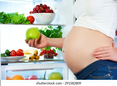 nutrition and diet during pregnancy. Pregnant woman standing near refrigerator with fruits and vegetables