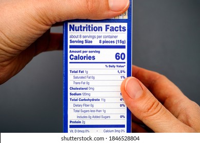 Nutrition facts on food box in woman hands. Gray background.