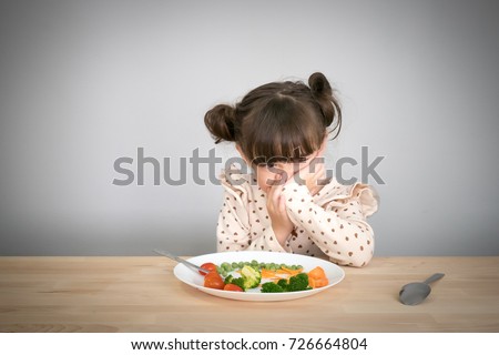 Nutrition & healthy eating habits for kids concept. Children do not like to eat vegetables. Little cute kid half race girl refuse to eat healthy vegetables.