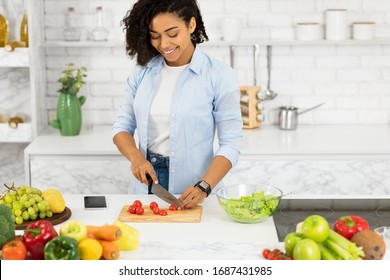 Nutrition Tips. Beautiful Black Girl Preparing Vegetable Salad At Home In Modern Loft Kitchen, Cutting Tomatoes, Copyspace