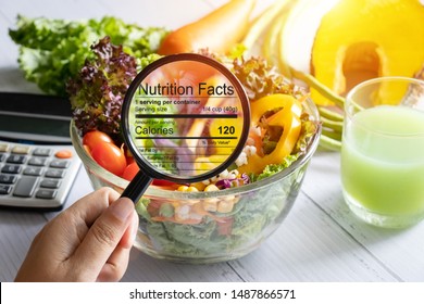 nutritional information concept. hand use the magnifying glass to zoom in to see the details of the nutrition facts from food , salad bowl