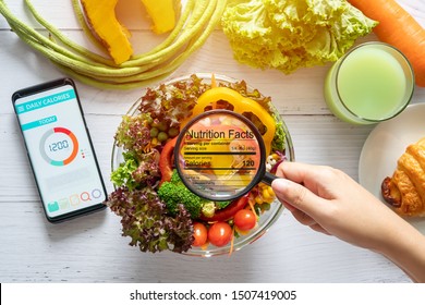 nutritional information concept. hand use the magnifying glass to zoom in to see the details of the nutrition facts from food , salad bowl - Shutterstock ID 1507419005