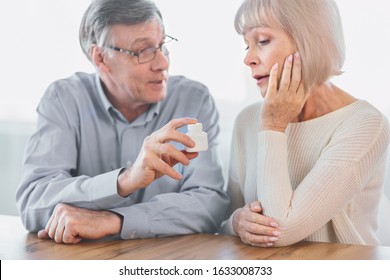 Nutritional Supplement. Smiling Senior Man Giving His Sad Wife New Prescription Bottle Sitting At Table