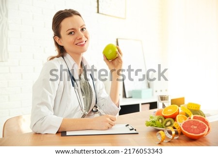 Nutritionist with apple and clipboard at desk in office