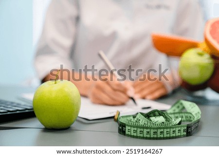 Nutritionist desk with healthy fruits, juice and measuring tape. Unrecognizable dietitian working on diet plan for overweight patient . Weight loss and right nutrition concept, selective focus