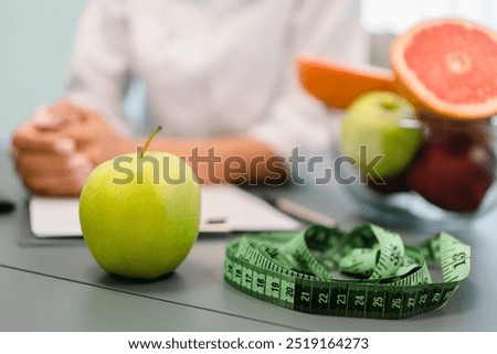 Nutritionist desk with healthy fruits, juice and measuring tape. Unrecognizable dietitian working on diet plan. Weight loss and right nutrition concept, selective focus
